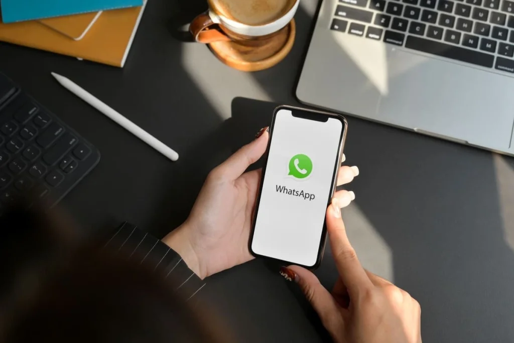 Mãos segurando celular na mesa de trabalho com o aplicativo WhatsApp empresarial na tela.