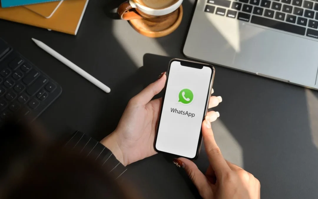 Mãos segurando celular na mesa de trabalho com o aplicativo WhatsApp empresarial na tela.