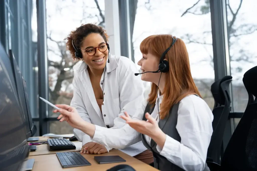 Atendentes de telemarketing sorrindo durante atendimento ao cliente em escritório.